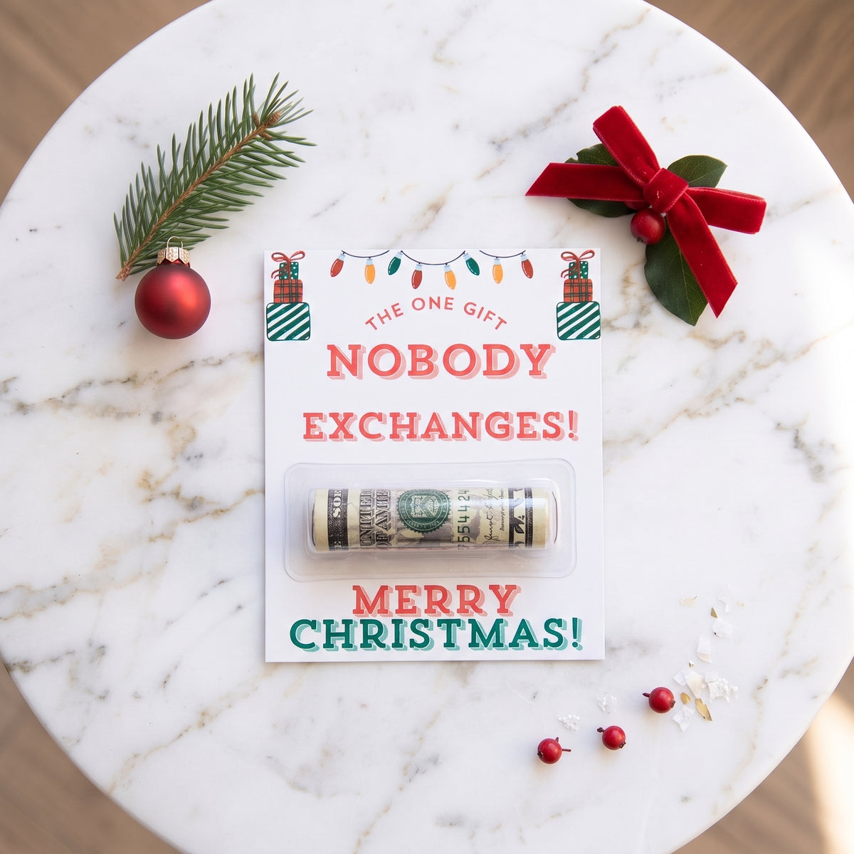 A rolled dollar bill sealed in a clear plastic tube, mounted on a white holiday card that reads 'The One Gift Nobody Exchanges! Merry Christmas!' The card is styled on a white marble surface with a green pine branch, red ornament, red ribbon, and small red berries.