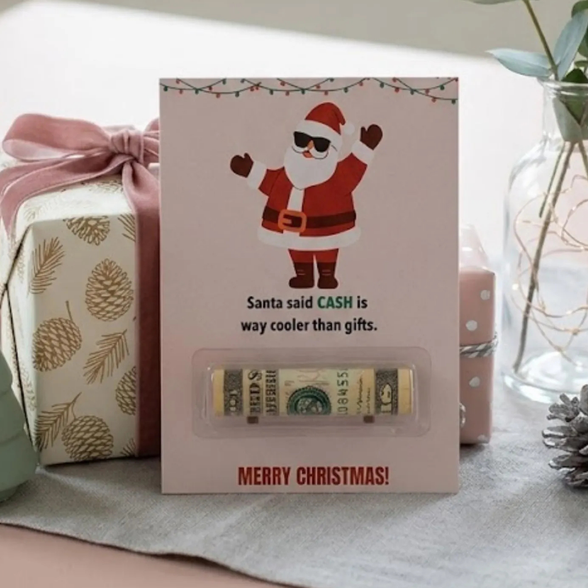 A Christmas-themed gift card holder or money box featuring a cartoon Santa Claus on a light pink card, with the text 'Santa said CASH is way cooler than gifts.' and 'MERRY CHRISTMAS!' at the bottom.