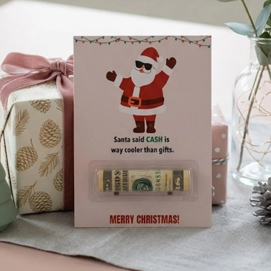 A Christmas-themed gift card holder or money box featuring a cartoon Santa Claus on a light pink card, with the text 'Santa said CASH is way cooler than gifts.' and 'MERRY CHRISTMAS!' at the bottom.