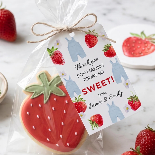 A strawberry-shaped sugar cookie wrapped in a clear cellophane bag with a personalized gift tag tied around the top. The tag features illustrations of strawberries, blue overalls, and the text 'Thank you FOR MAKING TODAY SO SWEET! Love, James & Emily'.
