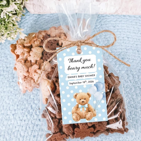 A clear cellophane gift bag filled with assorted cookies tied with twine and a printed thank-you tag, placed on a light blue textured surface with small flowers in the corner.