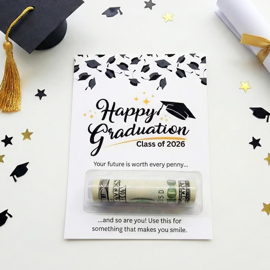 A graduation-themed money roll gift card on a white background with scattered black and gold graduation cap and star decorations. The card reads 'Happy Graduation Class of 2026' and includes a clear window showing a rolled dollar bill inside.
