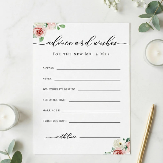 A square white wedding advice and wishes card with elegant black script and floral watercolor accents in pink, red, and green, styled on a white marble surface with candles, greenery, and a gold pen.