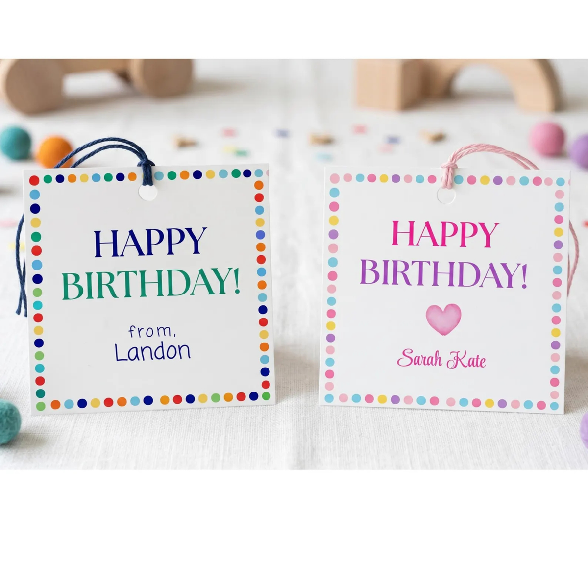 Two personalized birthday gift tags with colorful polka dot borders, displayed on a white surface with soft blurred party decorations in the background. One tag has a blue string and reads 'HAPPY BIRTHDAY! from.