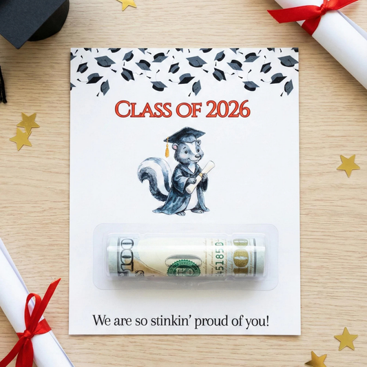 A graduation-themed card or envelope on a light wood surface, featuring the text 'CLASS OF 2026,' a cartoon squirrel in a graduation cap, and a clear plastic window holding a rolled $100 bill. The card reads 'We are so stinkin' proud of you!' at the bottom.