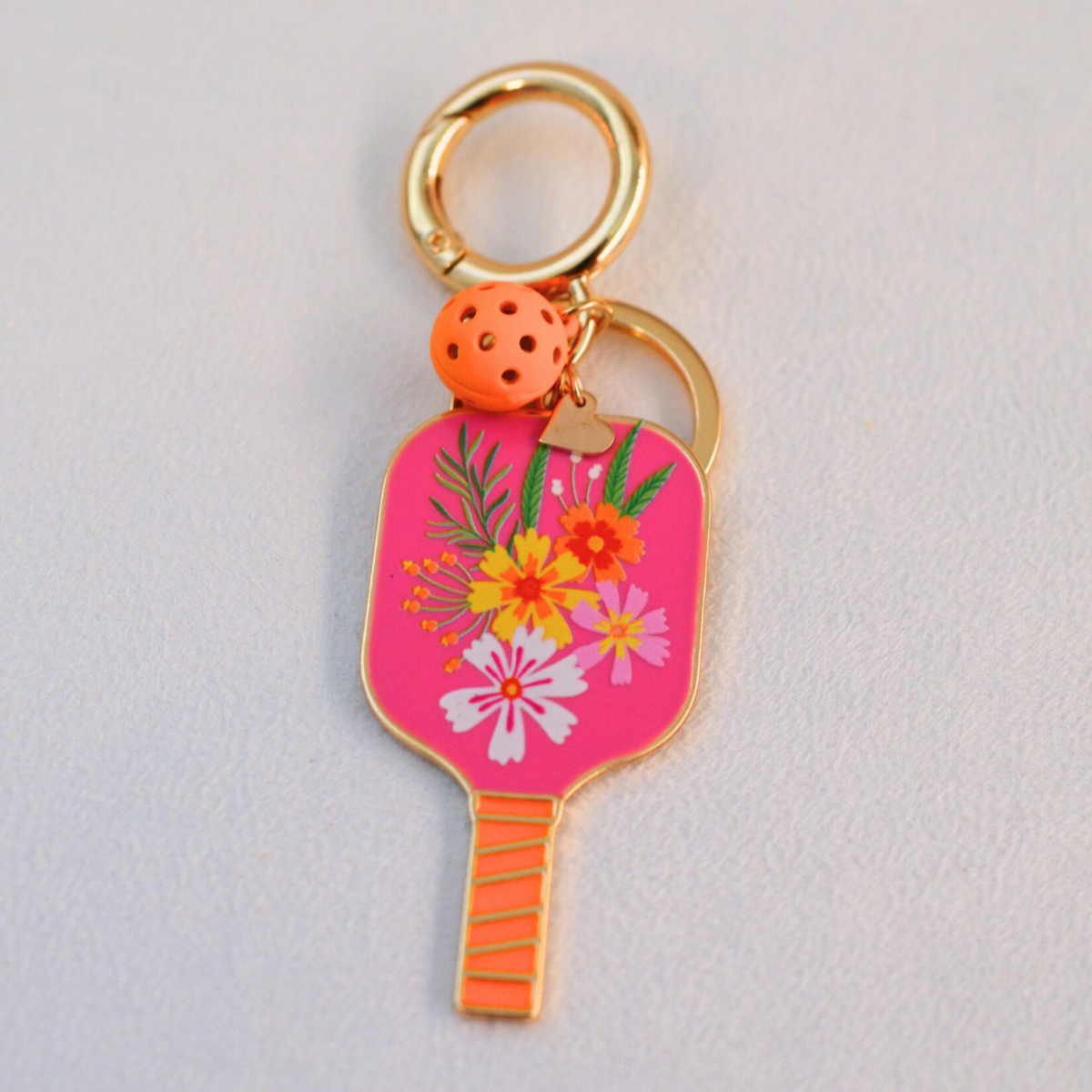Bright pink floral pickleball keychain with orange pickle ball displayed on a white backgroud.