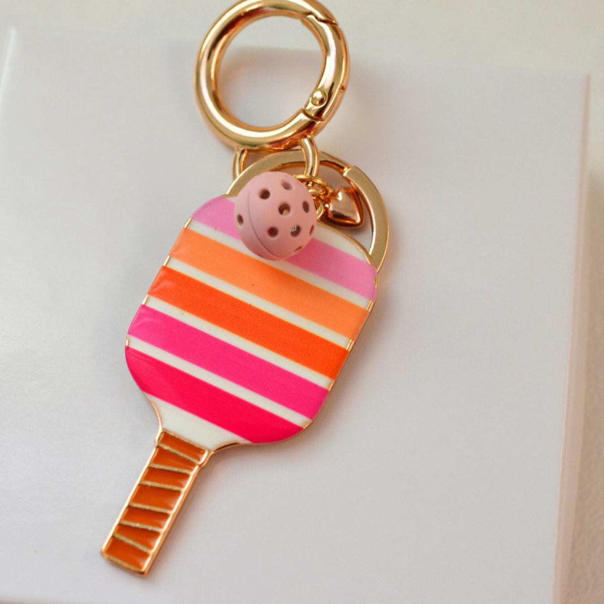 A novelty keychain shaped like a paddle-shaped popsicle with gold-tone metal trim and a small pink strawberry charm, shown on a clean white background.