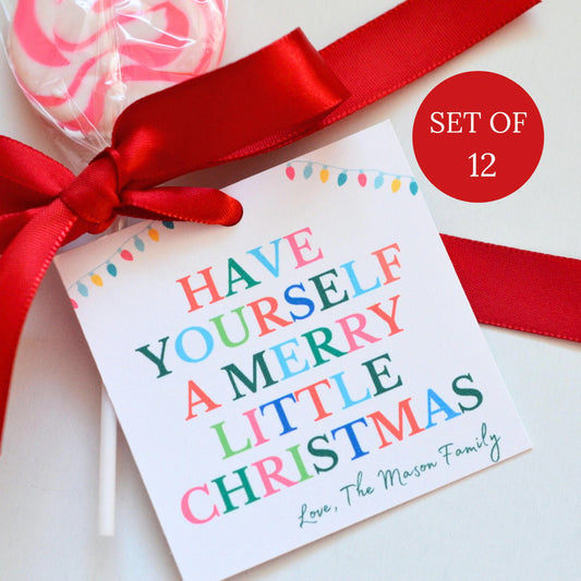 A set of personalized Christmas lollipop gift tags with a red ribbon and a pink and white lollipop, featuring the text 'HAVE YOURSELF A MERRY LITTLE CHRISTMAS' and 'Love, The Mason Family'. A red circular badge reads 'SET OF 12'.