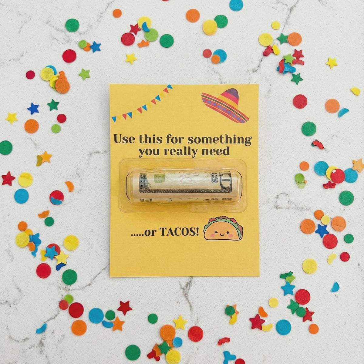 A rolled dollar bill tucked inside a clear plastic blister on a yellow card that reads 'Use this for something you really need' and '.