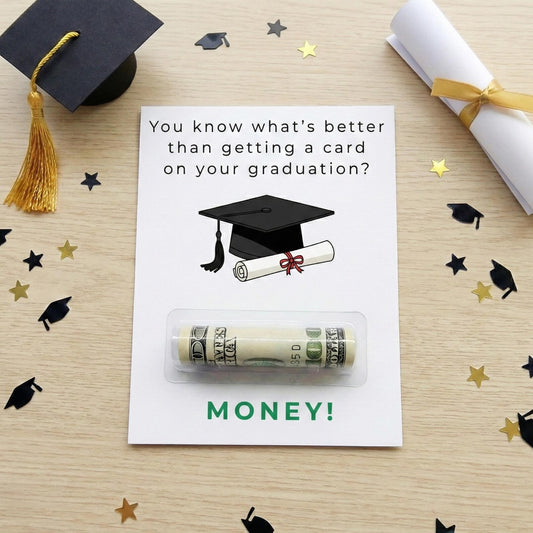 A graduation-themed money card on a light wood tabletop, surrounded by black and gold confetti and styled with a graduation cap, rolled diploma, and gold tassel. The card reads, 'You know what's better than getting a card on your graduation? MONEY!' with an illustration of a graduation cap and rolled diploma above a clear blister pack containing a rolled dollar bill.